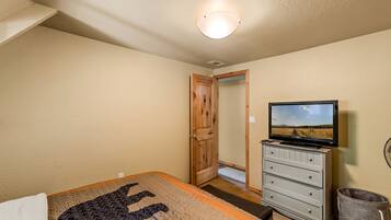 A bedroom with a bed, a dresser, a television, and a door leading to another room.