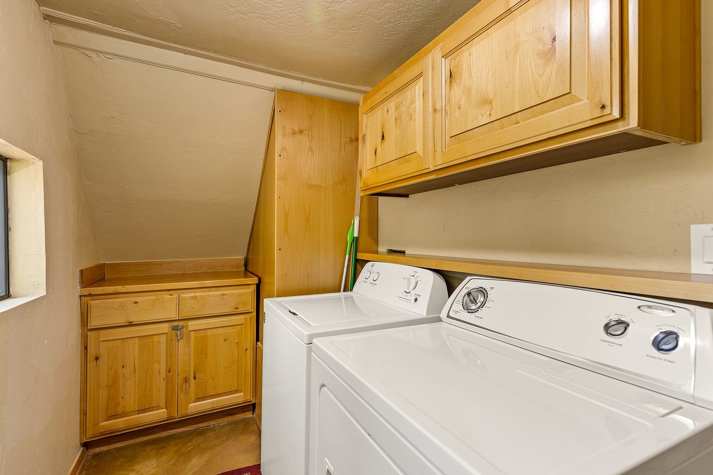 A laundry room with wooden cabinets and a front-loading washer and dryer.