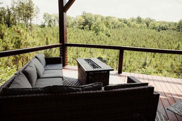 Un balcon avec un canapé en osier et une petite table, donnant sur une zone boisée.