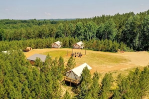 Un terrain de camping doté de plusieurs tentes et de cabanes, le tout entouré d’une forêt dense.
