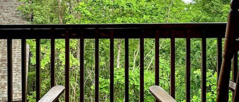 Une terrasse en bois avec deux chaises et une petite table, entourée d’arbres verdoyants.