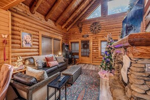 A log cabin interior with a fireplace, a Christmas tree, a sofa, and a clock on the wall. - Idyllic Mountain Retreat with Spa, Pool and Deck in Tennessee (Pigeon Forge)