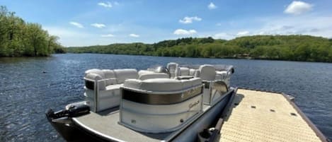 A boat docked at a wooden pier with a view of a forested shoreline.