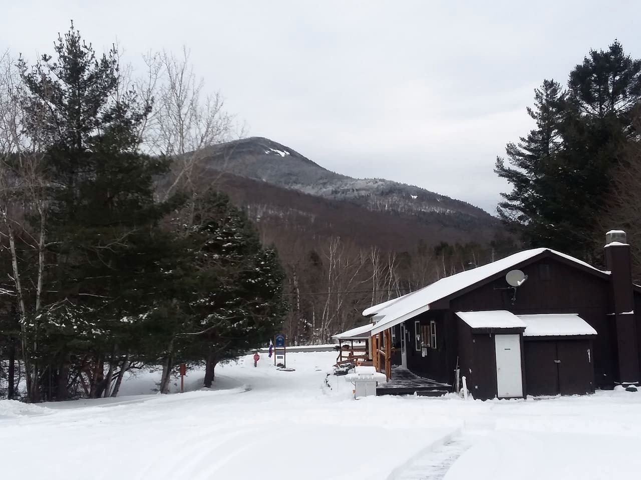 Un chalet enneigé, avec une façade en bois, une antenne parabolique et un toit recouvert de neige.