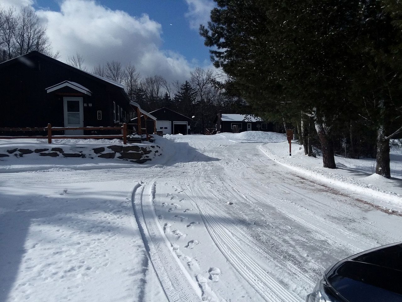 Uma estrada coberta de neve, com casas e árvores ao fundo.