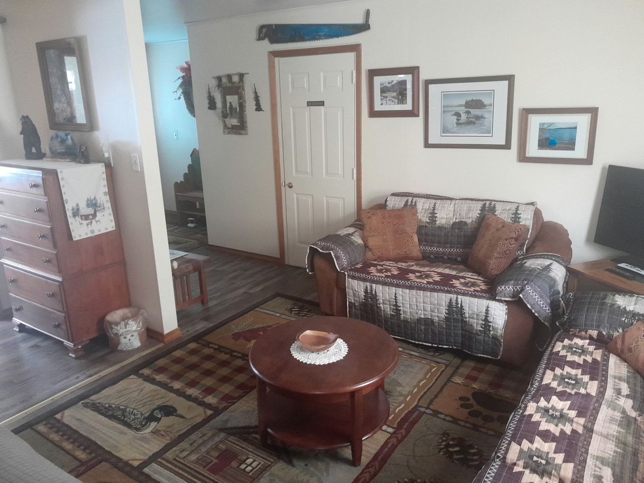 Un salon avec un canapé, une table en bois, un tapis à motifs et une porte.