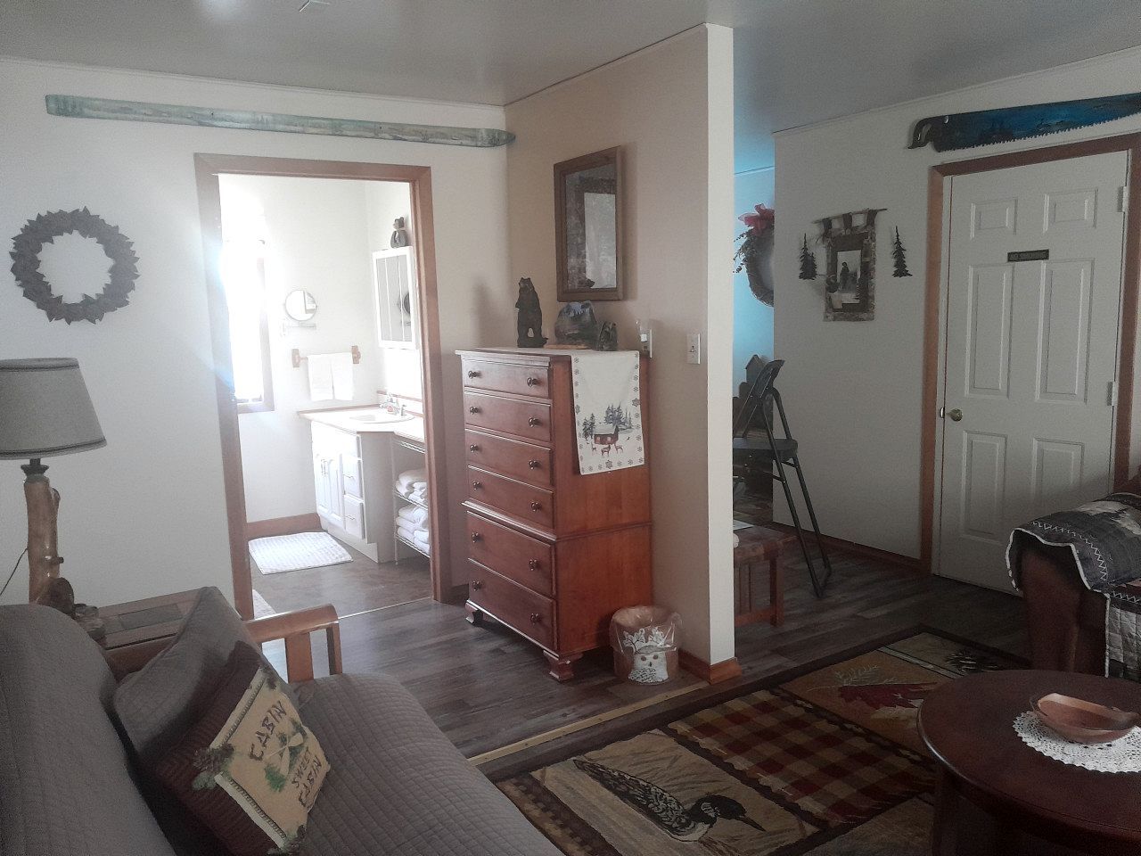 Uma sala de estar com um sofá, um aparador de madeira, uma mesinha e uma porta que dá para outro cômodo.