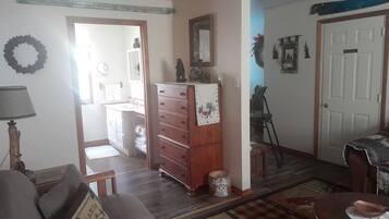 Uma sala de estar com um sofá, um aparador de madeira, uma mesinha e uma porta que dá para outro cômodo.