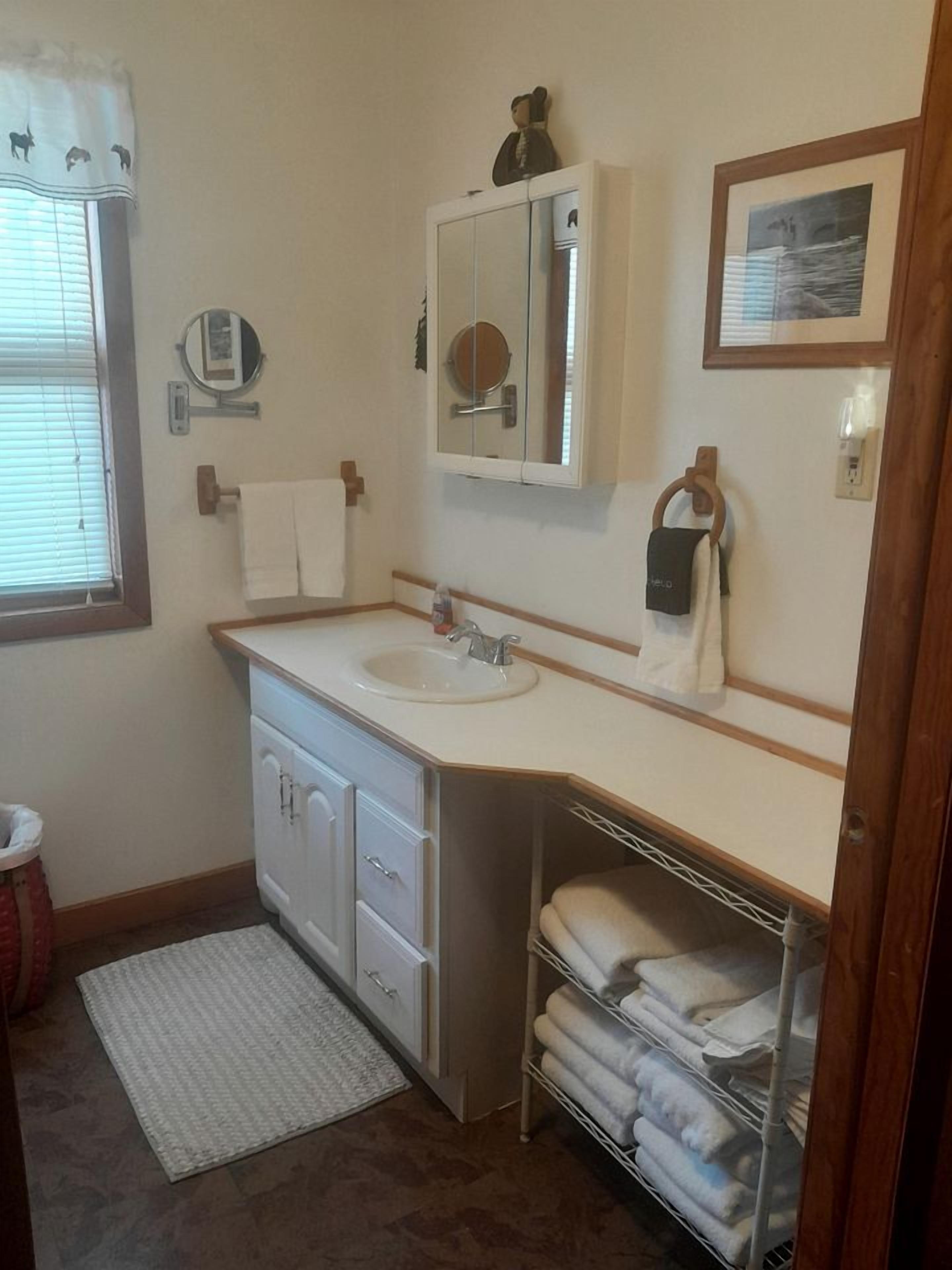 A bathroom with a sink, mirror, towel rack, and a shelf with folded towels.