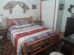 Quarto com cama de madeira, mesa de cabeceira, luminária, cômoda e porta.