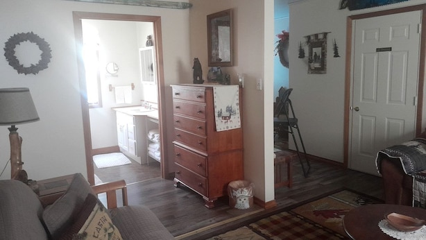Olohuoneessa on sohva, puinen lipasto, pieni pöytä ja ovi, joka johtaa toiseen huoneeseen.