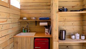 A compact kitchen with wooden walls, a sink, a red refrigerator, and various kitchen utensils and appliances. - Beautiful Secluded Yurt with Hot Tub in Dripping Springs, Texas (Dripping Springs)