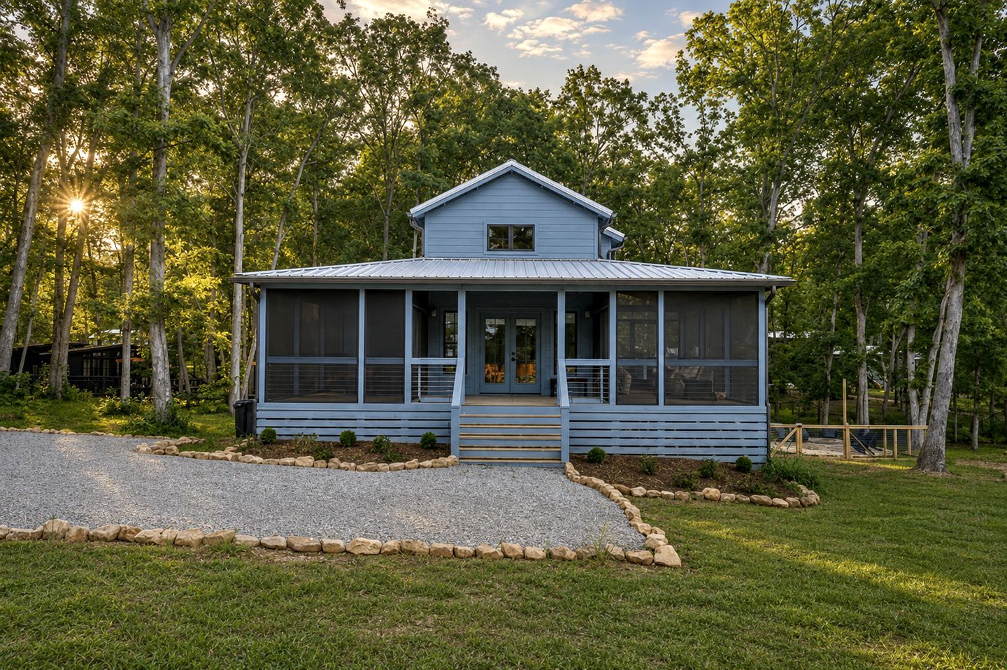 A single-story house with a porch, surrounded by trees and a gravel driveway.