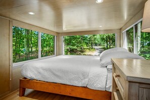 A bedroom with a wooden bed, a wooden nightstand, and large windows offering a view of a forest. - Glorious Lofted Container with Luxurious Indoor and Outdoor Spaces in Alabama (Mentone)