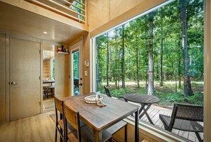 Un interior modern amb taula de dinar de fusta, cadires i una finestra gran amb vista a un bosc.