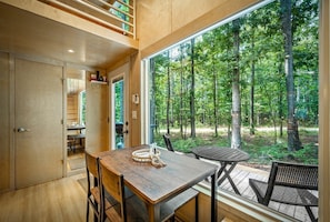 Un interior moderno con una mesa de comedor de madera, sillas y un amplio ventanal con vistas a un bosque.
