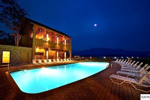 Ein Poolbereich mit Liegestühlen, ein mehrgeschossiges Gebäude und ein Nachthimmel.