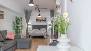 A modern living room with a sofa, a dining table, and a white vase with flowers. - Vacation Studio 'Vv Ancla' with Mountain View, Wi-Fi and Air Conditioning (Puerto de Mogán)