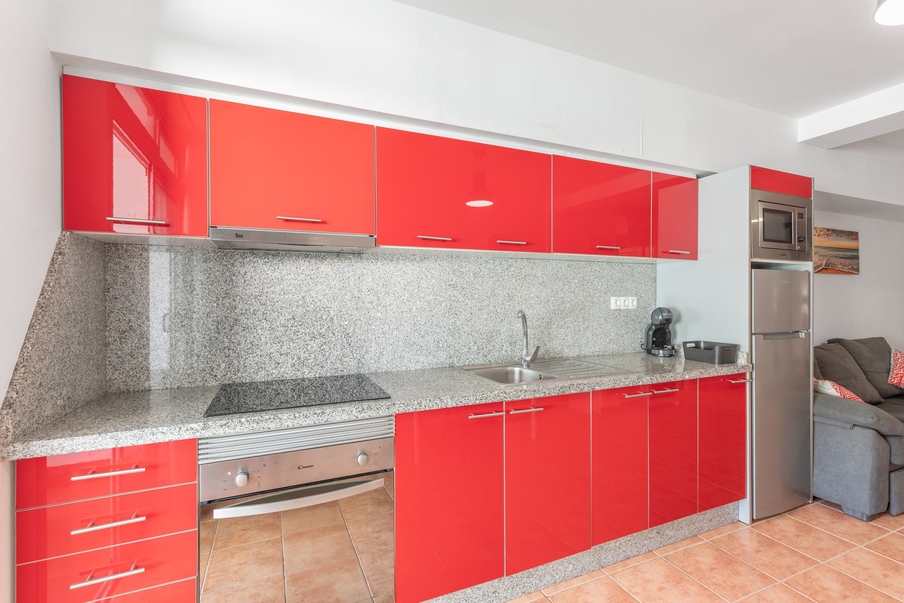 Une cuisine avec des meubles de couleur rouge, un réfrigérateur en acier inoxydable et un plan de travail en granit.