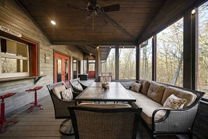 A covered outdoor seating area with a table and chairs, a sofa, and a view of trees. - Stunning Cabin with Games Perfect for Families in Broken Bow, Oklahoma (Broken Bow)