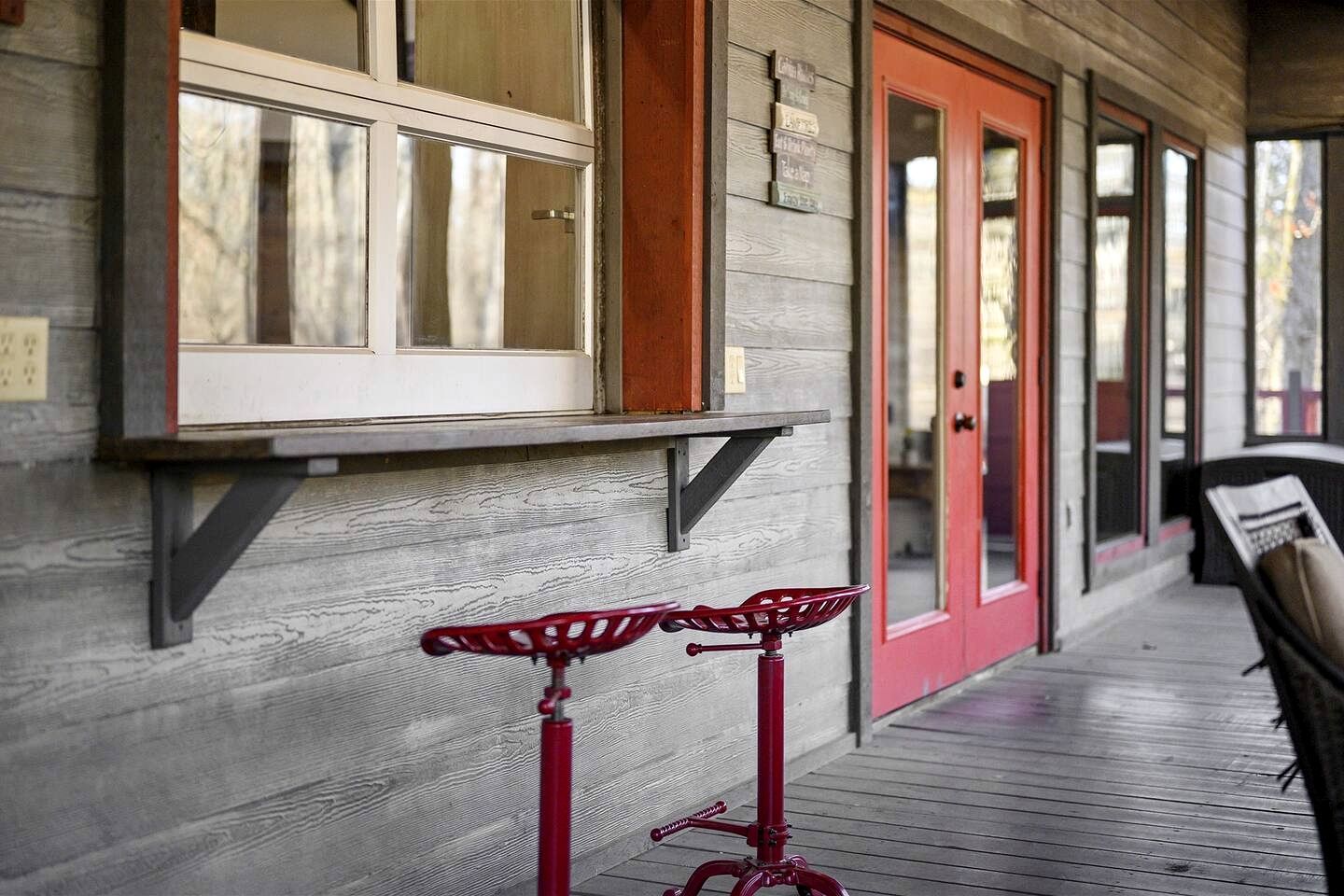 A wooden porch with a red door, a window, and a red bicycle.