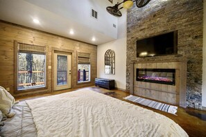 A bedroom with a large bed, a fireplace, and a view through a window. - Stunning Cabin with Games Perfect for Families in Broken Bow, Oklahoma (Broken Bow)