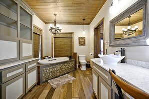 A bathroom with a large mirror, a freestanding bathtub, a toilet, and a vanity with a sink. - Stunning Cabin with Games Perfect for Families in Broken Bow, Oklahoma (Broken Bow)