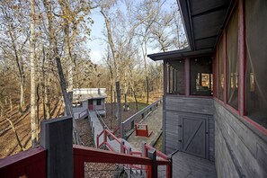 Eine Holzhütte mit einem Balkon, einem kleinen Anbau und bewaldeter Umgebung.