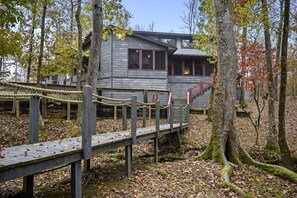 Un chalet rustique doté d’une terrasse en bois, entouré d’arbres et délimité par une barrière en corde.