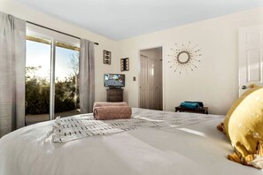 A bedroom with a large bed, a TV, a sunburst wall decoration, and a sliding glass door to a balcony. - Yucca Valley Wonderland: Embark on a Unique Desert Adventure (Yucca Valley)