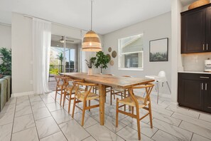 A modern kitchen with dark cabinets, a wooden dining table, and a hanging pendant light. - 7BR Lakeview Villa + Heated Pool | 15min to Disney (Kissimmee)