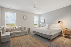 Une chambre à coucher comprenant un lit, un canapé, une lampe sur pied et un ventilateur de plafond.