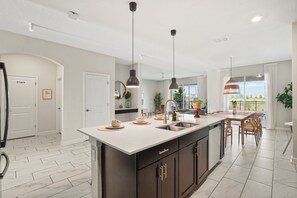 A modern kitchen with a large island, pendant lights, and a dining area with a view. - 7BR Lakeview Villa + Heated Pool | 15min to Disney (Kissimmee)