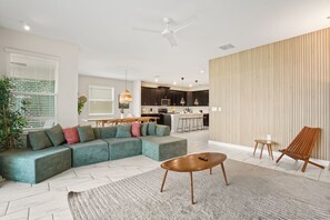 A modern living room with a sectional sofa, a coffee table, and a dining area with a kitchen in the background. - 7BR Lakeview Villa + Heated Pool | 15min to Disney (Kissimmee)