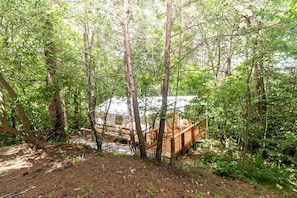 Une zone boisée avec une terrasse en bois et un bâtiment blanc.