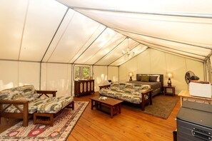 A tented accommodation with a bed, two sofas, a table, and a fan.