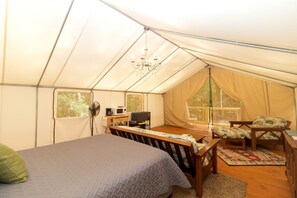 A tent with a bed, a desk, a chair, a fan, and a chandelier.