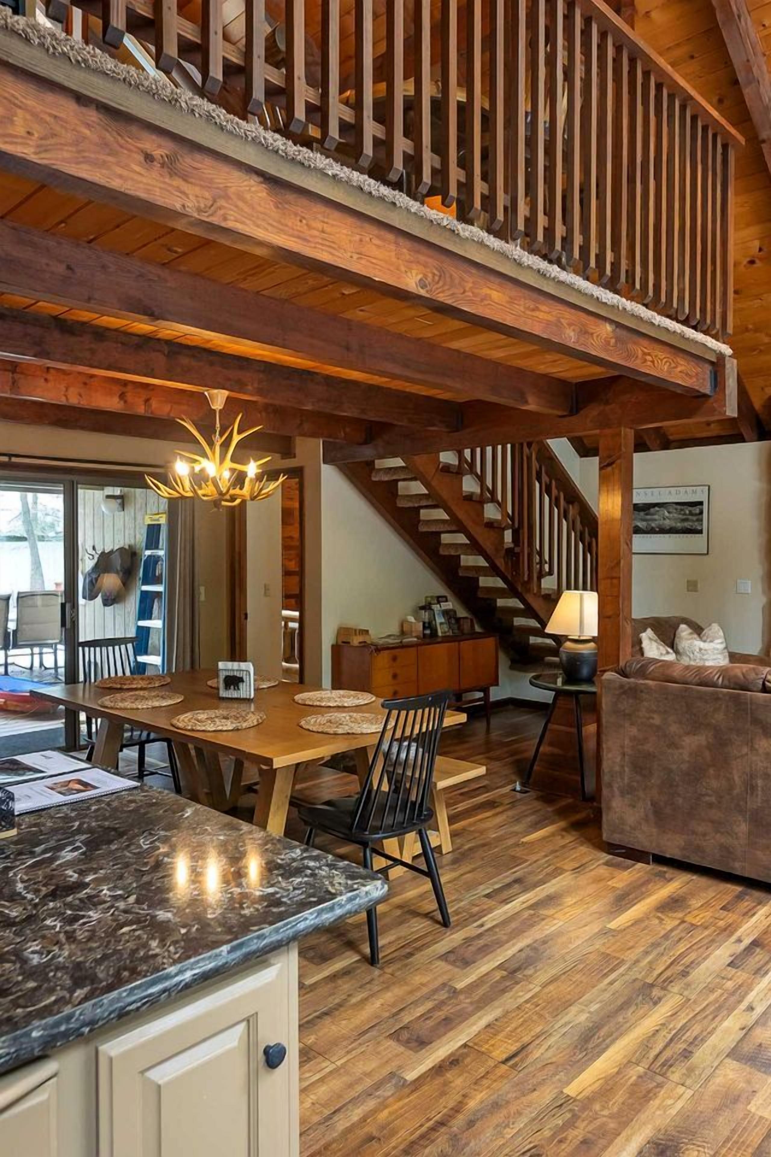 Uma sala ampla com escada de madeira, mesa de jantar com cadeiras, cozinha com bancada de mármore e um espaço de estar aconchegante com um sofá.