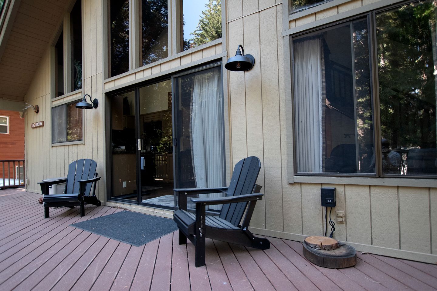 A wooden deck with two Adirondack chairs, a glass door entrance, and a mailbox.