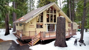 A cabin with a wooden deck, large windows, and a visible address sign. - Pinecone Cottage in Dorrington, CA (Dorrington)