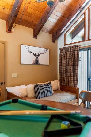 A cozy room with a pool table, a bed with striped pillows, a painting of an elk, and a plaid curtain. - Pinecone Cottage in Dorrington, CA (Dorrington)