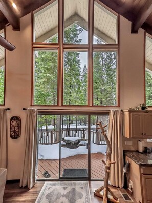 A high-ceilinged room with large windows, a wooden deck, and a rustic decor. - Pinecone Cottage in Dorrington, CA (Dorrington)