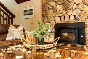 A fireplace with a stone wall, a wooden table with a woven basket, and a framed picture on the wall. - Pinecone Cottage in Dorrington, CA (Dorrington)