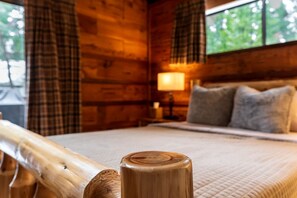 A wooden cabin room with a bed, a nightstand, and a window with curtains. - Pinecone Cottage in Dorrington, CA (Dorrington)