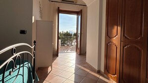 A hallway with a view to a balcony, a bed with a green bedspread, and a wooden wardrobe.