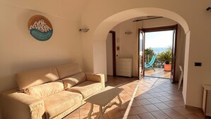 A spacious living room with a beige sofa, a small table, and a view of the outdoors through an arched doorway.