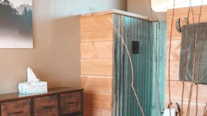 Uma cômoda de madeira com gavetas, uma pequena caixa de lenços de papel, uma parede de azulejos verdes e um vaso sanitário branco com um rolo de papel higiênico.