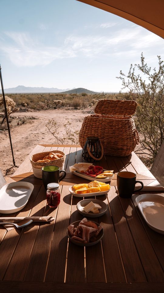A dining table set with food and drinks, a wicker basket, and a view of a desert landscape.