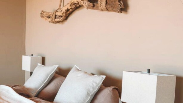 Quarto com cama, almofadas, um ornamento de madeira pendurado e luminárias de cabeceira.