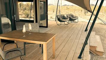 Una terraza de madera con una mesa, sillas, una tienda de campaña y vistas a un paisaje desértico.